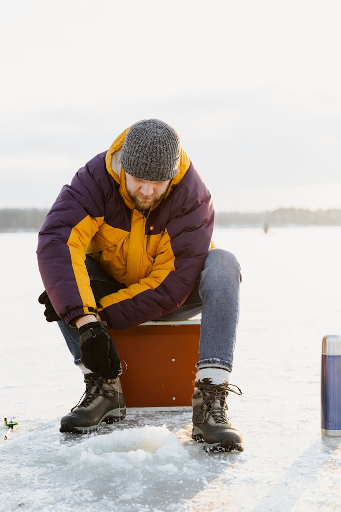 Man enjoying ice fishing on a snowy lake in winter attire.